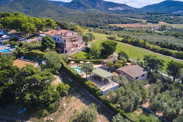 A large villa with a swimming pool, surrounded by lush greenery and mountains.