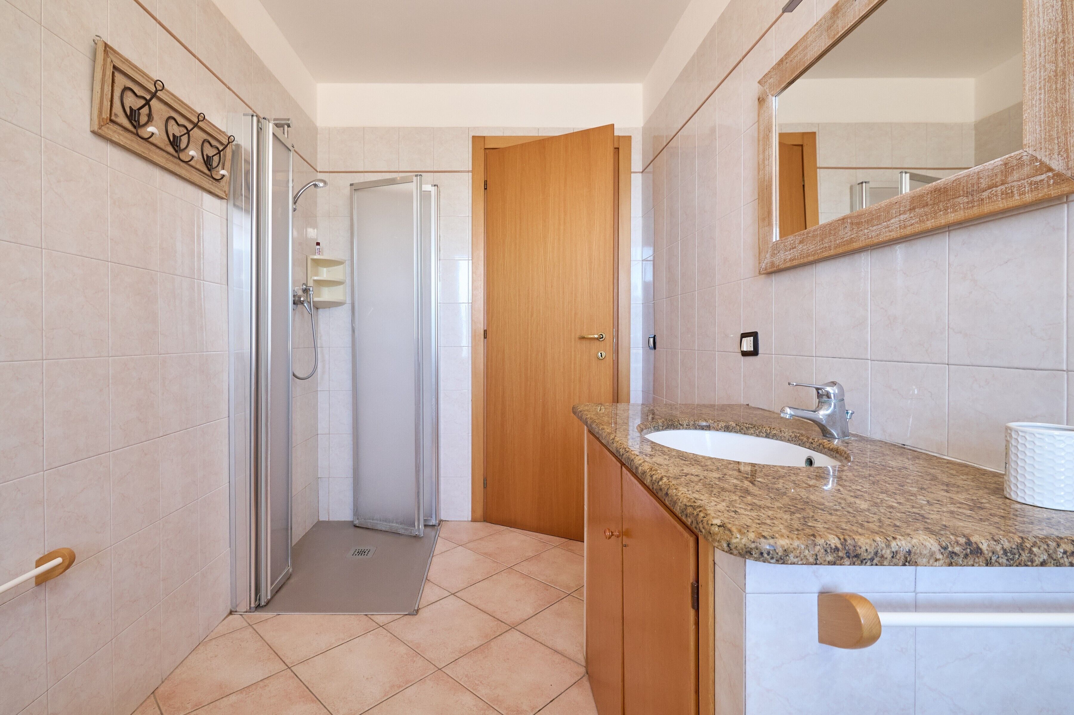 Bagno con doccia, lavandino, specchio e porta in legno.