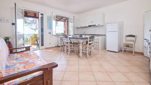 Una cocina con una mesa de comedor, sillas, un refrigerador y un sofá con un cojín colorido.
