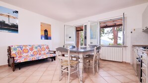 Un comedor con mesa y sillas, un banco, vista por una ventana y una zona de cocina.
