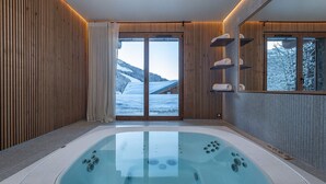Ein moderner Wellnessraum mit einer großen Whirlwanne, Holzwandverkleidung und Blick auf eine verschneite Landschaft.
