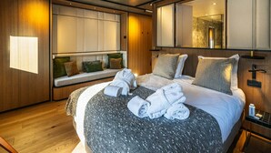 Ein modernes Hotelzimmer mit einem großen Bett, einer Sitzecke mit Kissen, Holzboden und einem großen Spiegel.
