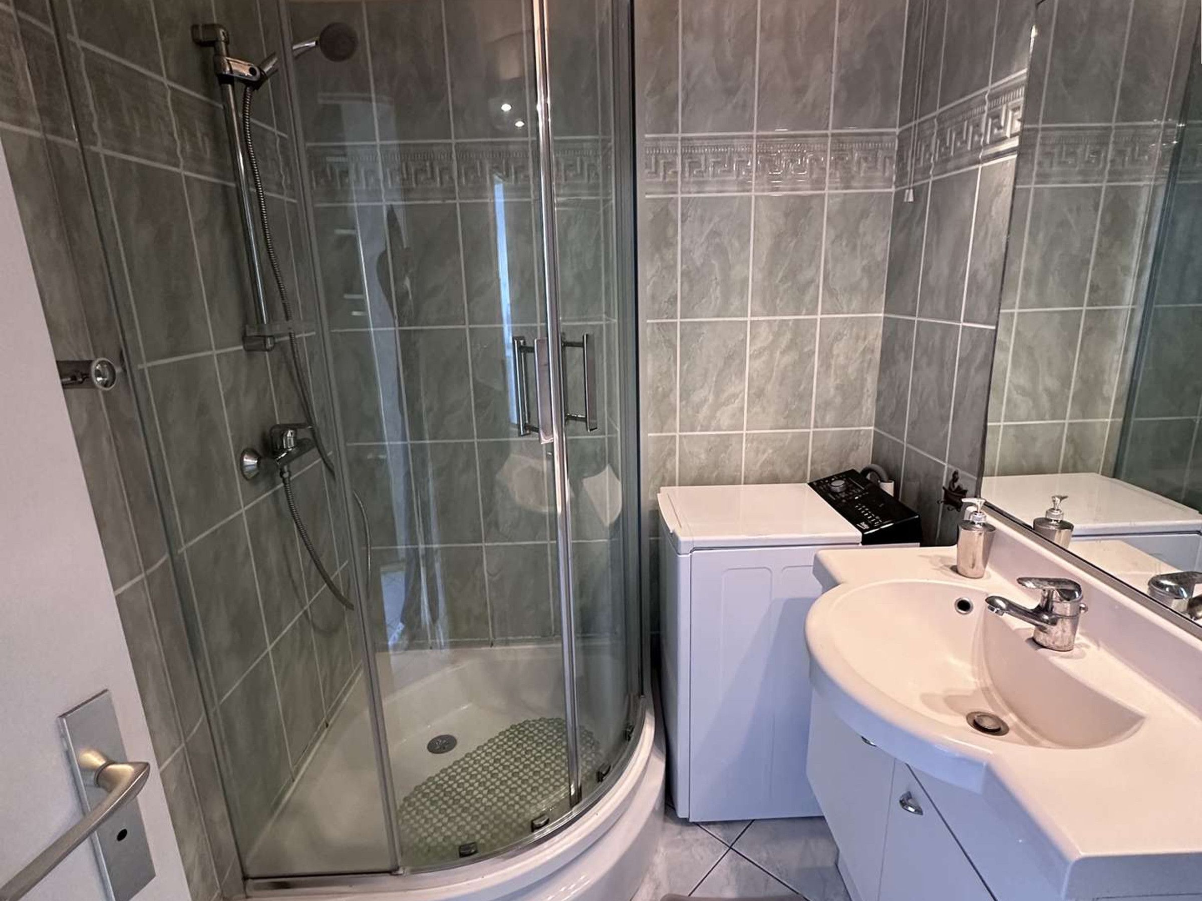 A modern bathroom with a glass-enclosed shower, a white sink, and a mirror.