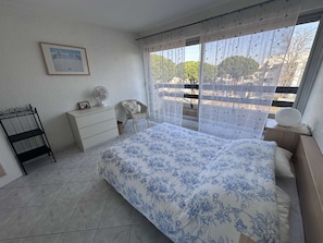 A bedroom with a bed, a dresser, a chair, a fan, and a window with a view of trees.