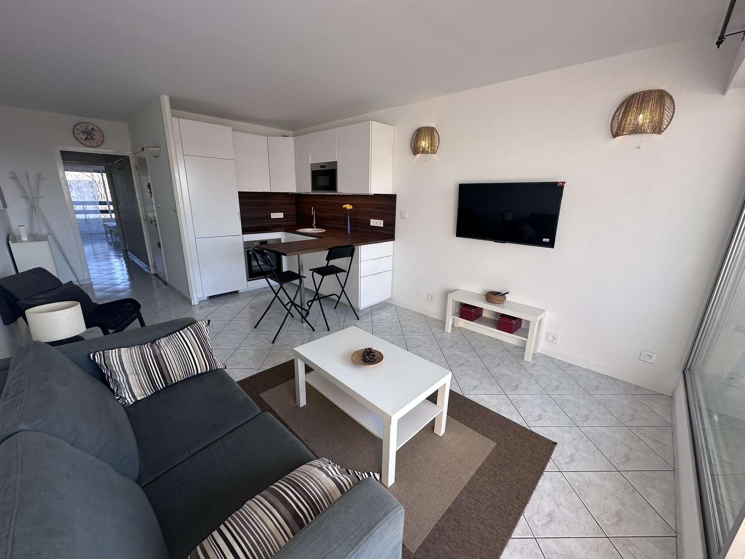 Een moderne woonkamer met een grijze bank, een salontafel en een aan de muur bevestigde televisie.