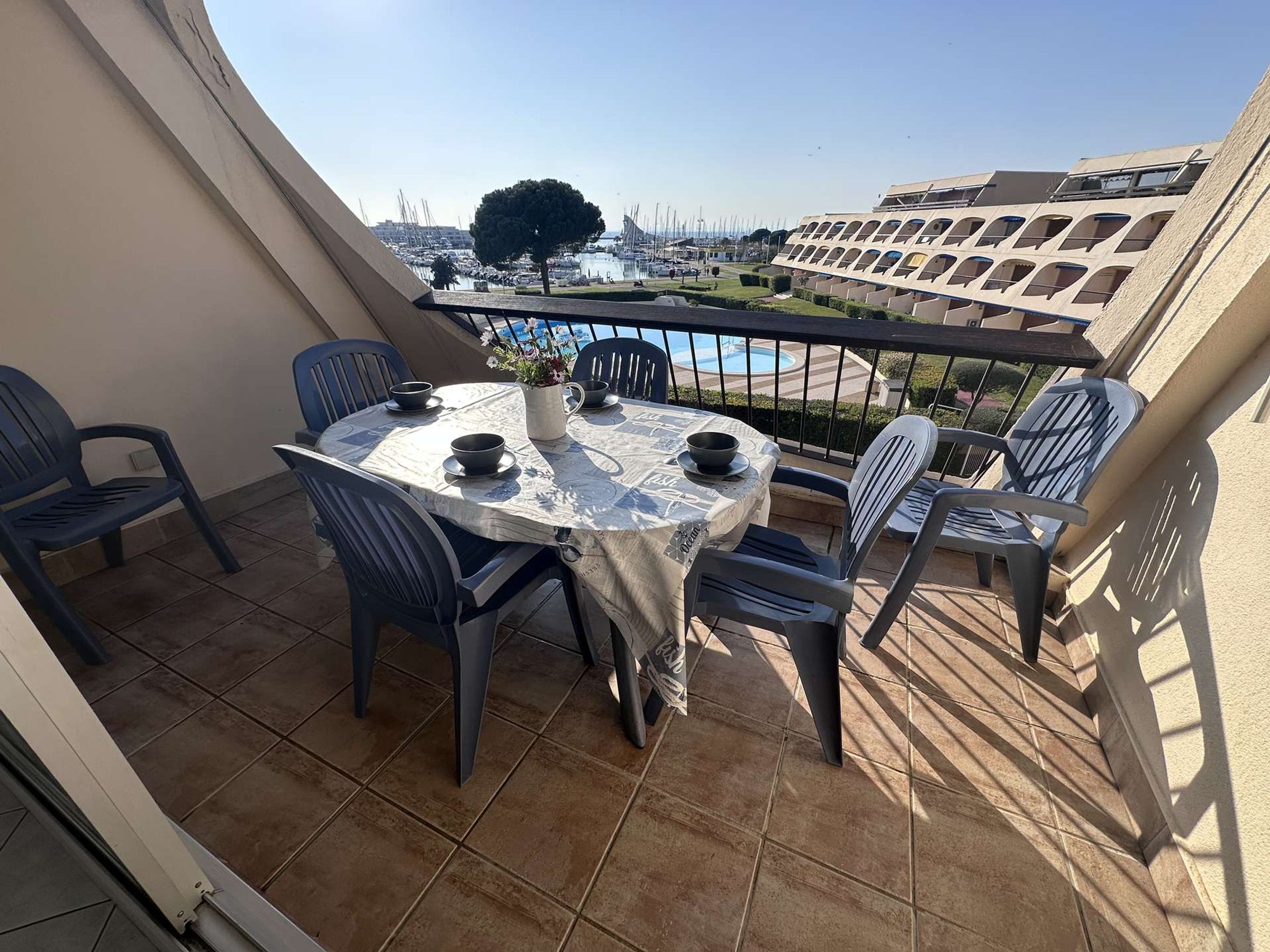 A balcony with a table and chairs, a view of a marina, and a building with a unique architectural design.