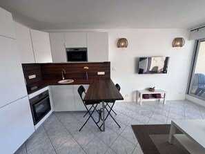 A modern kitchen with a dark wood countertop, white cabinets, a built-in microwave, and a dining area with a foldable table and chairs.