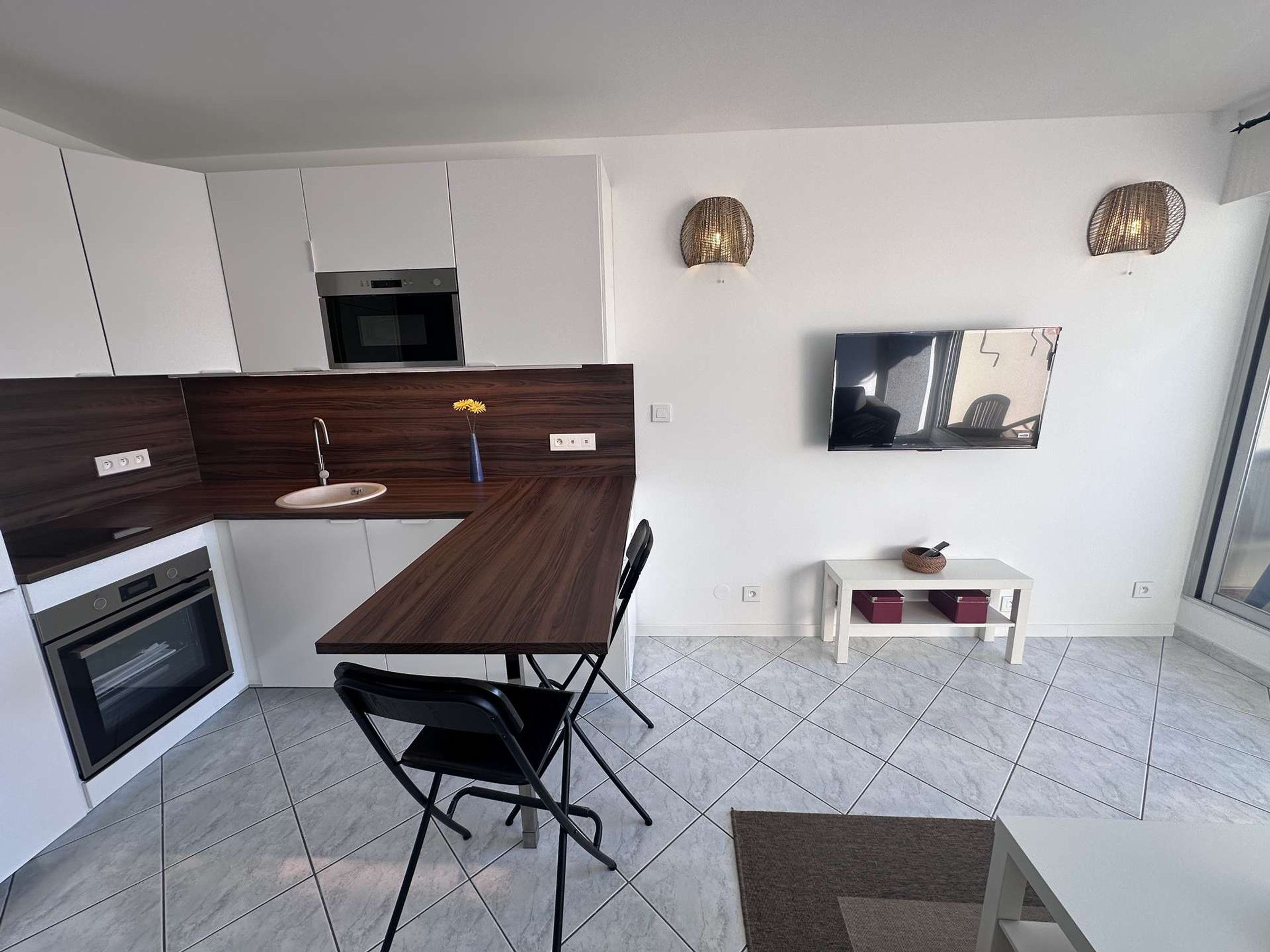 A modern kitchen with a dark wood countertop, white cabinets, a built-in oven, and a dining area with a black chair and a small table.