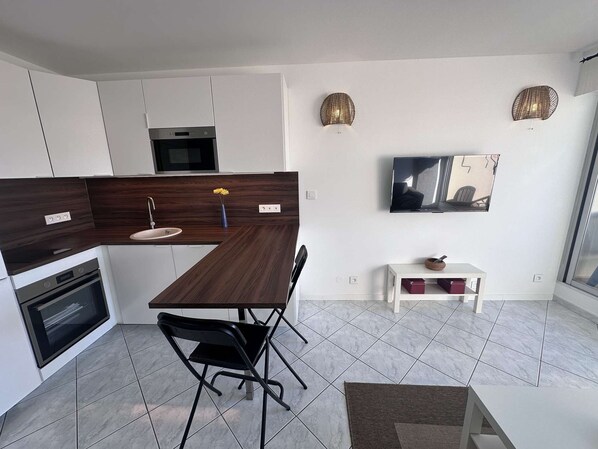 A modern kitchen with a dark wood countertop, white cabinets, a built-in oven, and a dining area with a black chair and a small table.