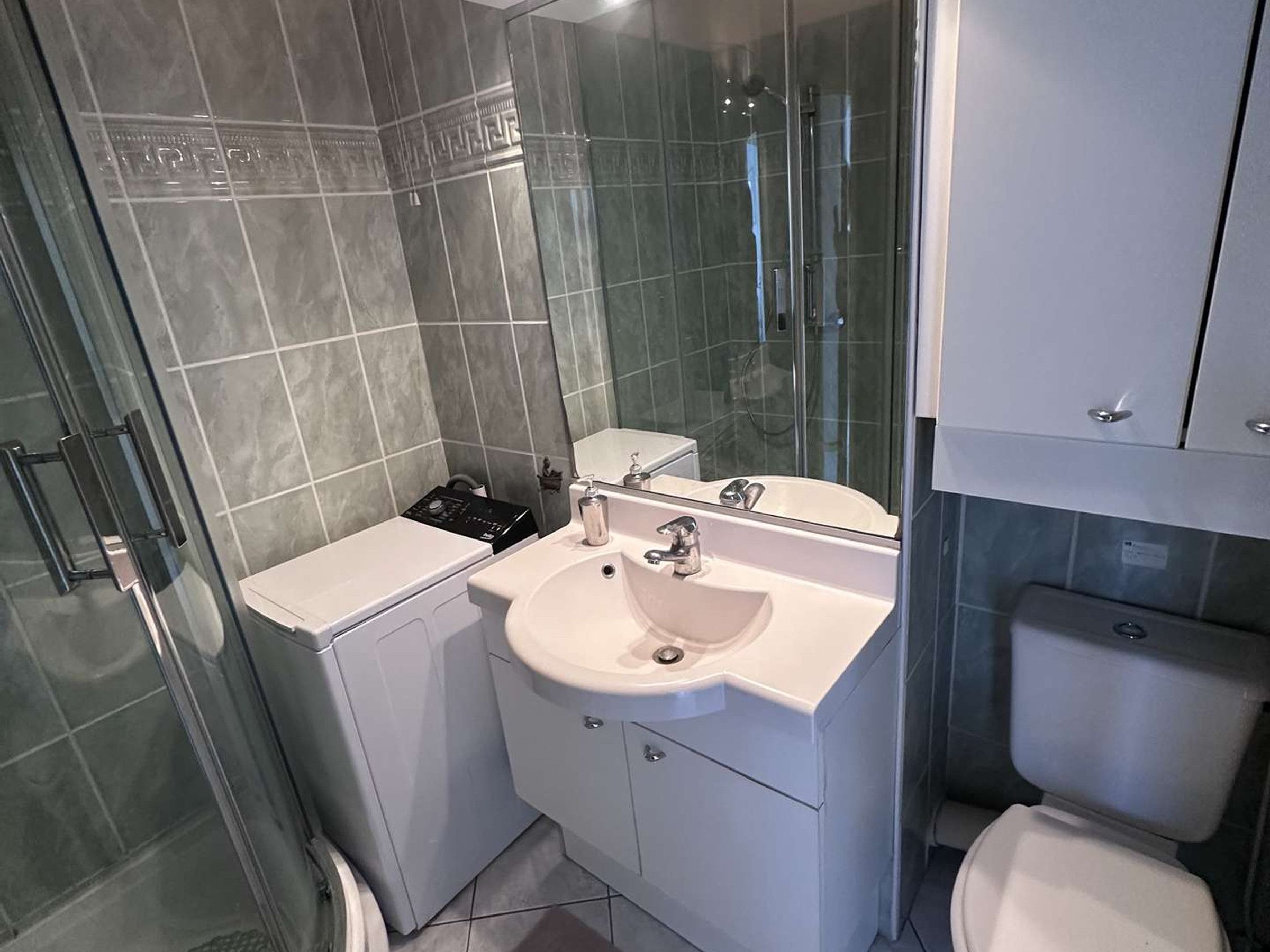 A bathroom with a glass shower enclosure, a white sink, a toilet, and a cabinet with a mirror.