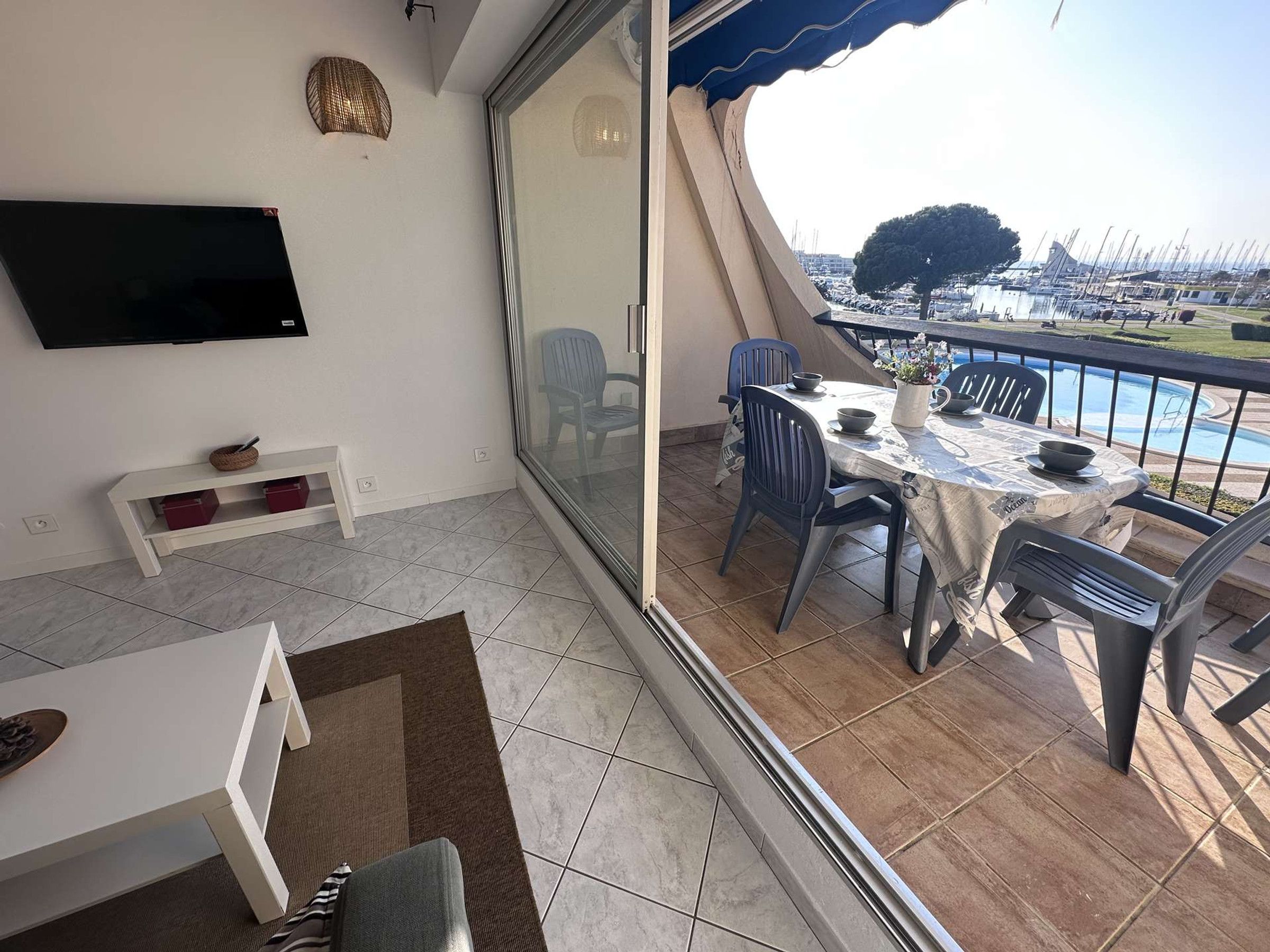 A balcony with a table and chairs, a television, and a view of a marina.