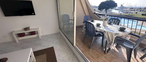 En balkong med ett bord och stolar, en tv och utsikt över en småbåtshamn.