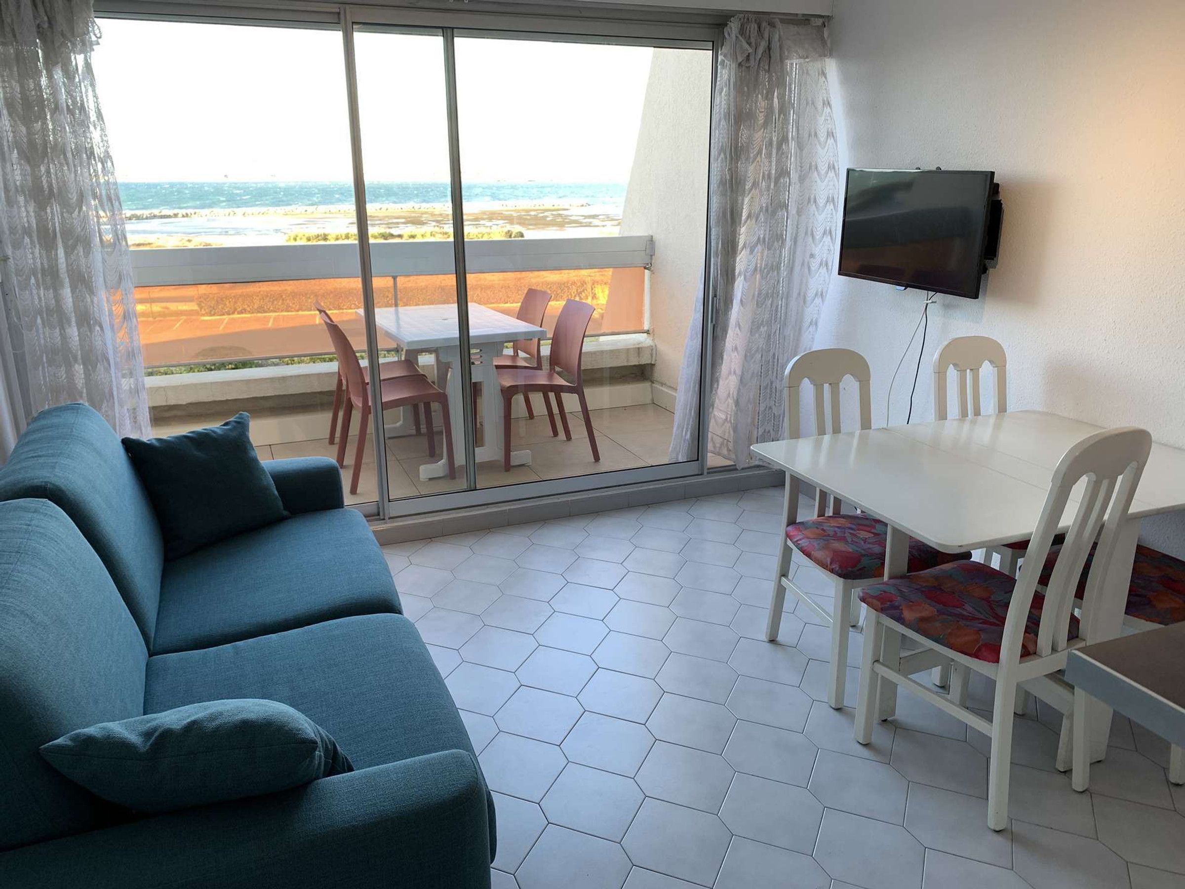 Ein Zimmer mit einer Couch, einem Esstisch mit Stühlen, einem an der Wand montierten Fernseher und Meerblick durch große Fenster.