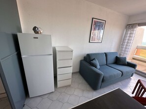 A compact living space with a white refrigerator, a grey sofa, and a small cabinet. - Sea view studio-cabin 50m from beach, private parking (Port Camargue)
