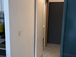 A hallway with a white wall, a door leading to a room with a dark door, and a tiled floor. - Sea view studio-cabin 50m from beach, private parking (Port Camargue)