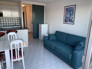 A compact living space with a kitchenette, a dining area with chairs, a sofa, and a wall-mounted artwork. - Sea view studio-cabin 50m from beach, private parking (Port Camargue)