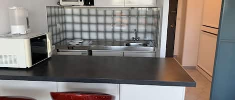 A compact kitchen with a microwave, stove, and sink. There are two red bar stools.