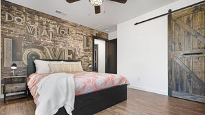 A bedroom with a bed, a nightstand, a wall with a 'DO WHAT YOU LOVE' mural, and a wooden door. - Beautiful Kitchen, BBQ, Outdoor Dining, Big Yard (St. Augustine)