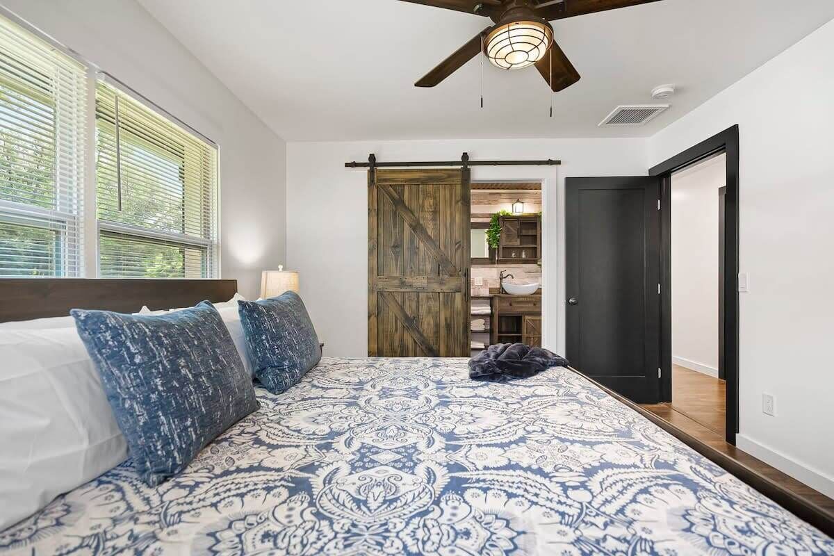 A bedroom with a large bed, a ceiling fan, a sliding barn door, and a view into the kitchen.