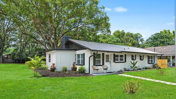 A single-story house with a white exterior, a dark roof, and a front porch with two chairs. - Beautiful Kitchen, BBQ, Outdoor Dining, Big Yard (St. Augustine)