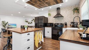 A modern kitchen with a wooden ceiling, brick wall, and white cabinetry. - Beautiful Kitchen, BBQ, Outdoor Dining, Big Yard (St. Augustine)
