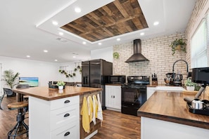 A modern kitchen with a wooden ceiling, brick wall, and white cabinetry. - Beautiful Kitchen, BBQ, Outdoor Dining, Big Yard (St. Augustine)