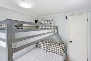 Un lit superposé avec une literie à carreaux et une porte blanche en arrière-plan.
