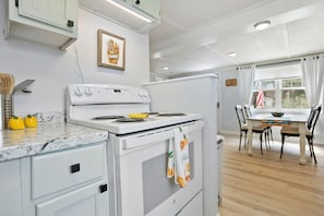 A kitchen with white appliances, a marble countertop, and a dining area with a table and chairs. - Qt Cottage on Dunn's Creek, Fire Pit, Kayaks (Satsuma)