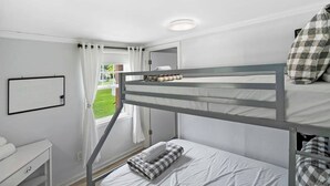Habitació amb literes, escriptori blanc i finestra amb cortines.