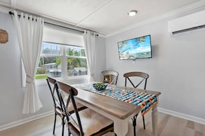 A dining area with a wooden table, two chairs, a bowl, and a painting on the wall. - Qt Cottage on Dunn's Creek, Fire Pit, Kayaks (Satsuma)