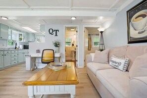 A modern living room with a wooden coffee table, a beige sofa, and a wall-mounted painting of a coffee cup. - Qt Cottage on Dunn's Creek, Fire Pit, Kayaks (Satsuma)