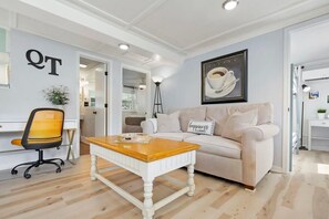 Una sala de estar moderna con un sofá blanco, una mesa de centro de madera y un cuadro de una taza de café en la pared.