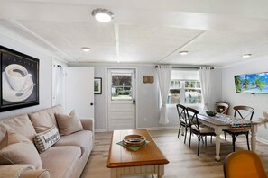 A living room with a sofa, a coffee table, and a dining area with chairs and a table. - Qt Cottage on Dunn's Creek, Fire Pit, Kayaks (Satsuma)