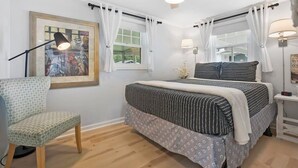 Ein Schlafzimmer mit einem Bett, einem Sessel, einem Deckenventilator und einem Fenster mit Vorhängen.