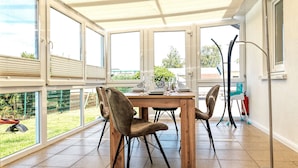 A dining area with a table set for four, surrounded by chairs, large windows, and a ceiling fan. - Bungalow LAETITIA - In a peaceful central location in Timmendorf Strand. (Insel Poel / OT Timmendorf Strand)
