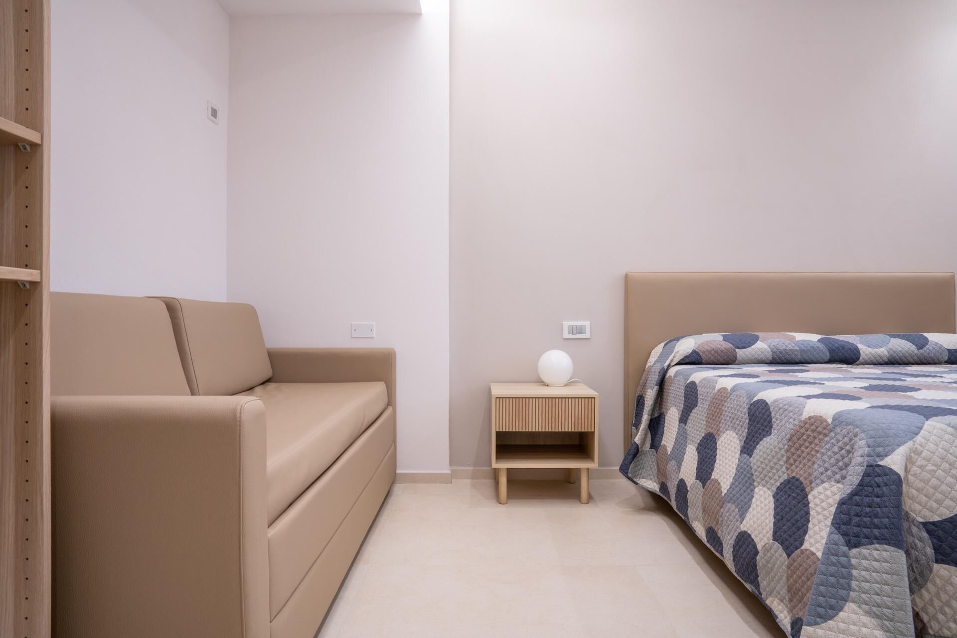 Ein Schlafzimmer mit einem Bett, einem Nachttisch, einer Couch und einer wandmontierten Leuchte.