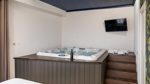A modern bathroom with a built-in jacuzzi, a flat-screen TV, and a wooden vanity.