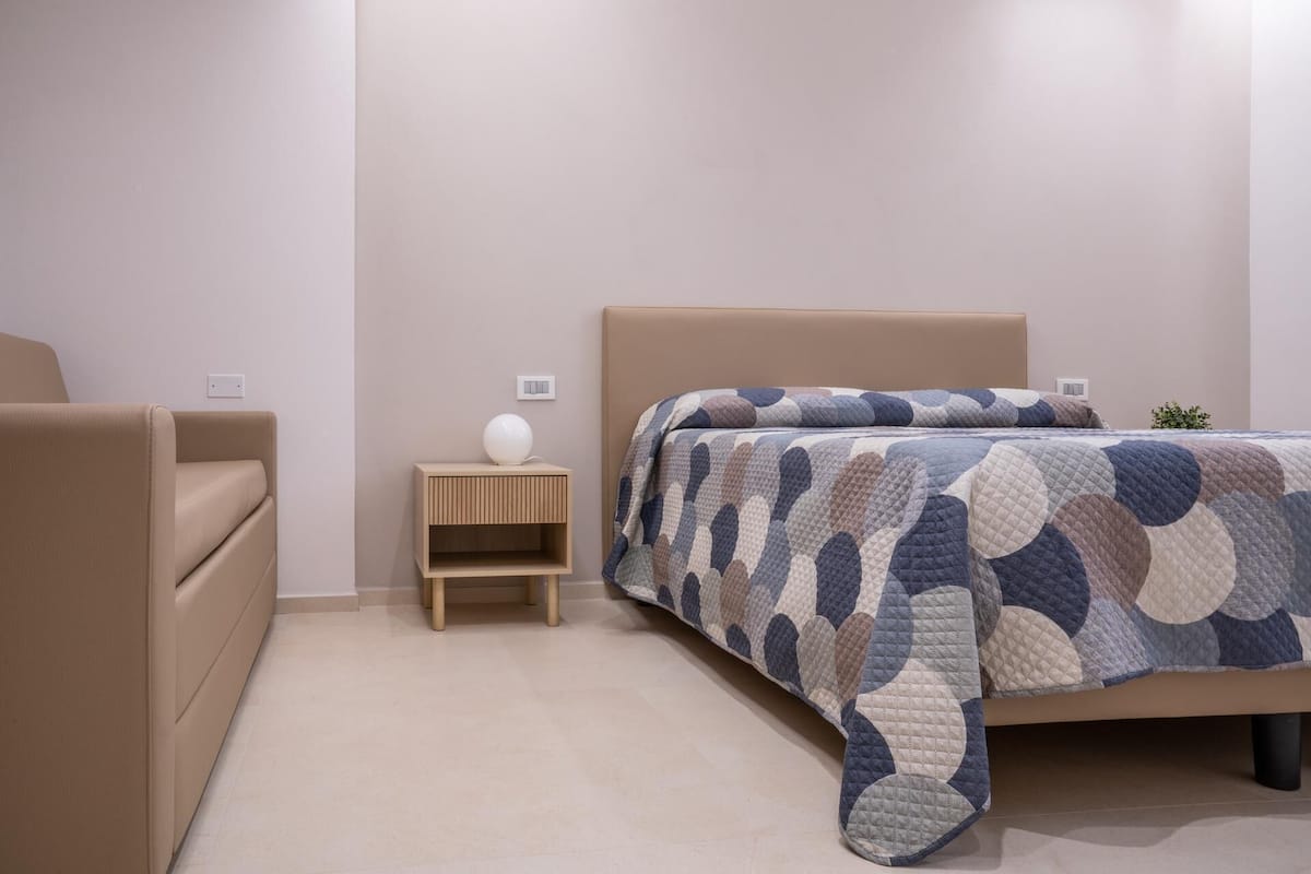 Ein Schlafzimmer mit einem Bett, einem Nachttisch, einer Lampe und einem Sessel.