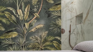 A room with a bed, a shower area with a marble wall, and a tropical leaf pattern on the wall.