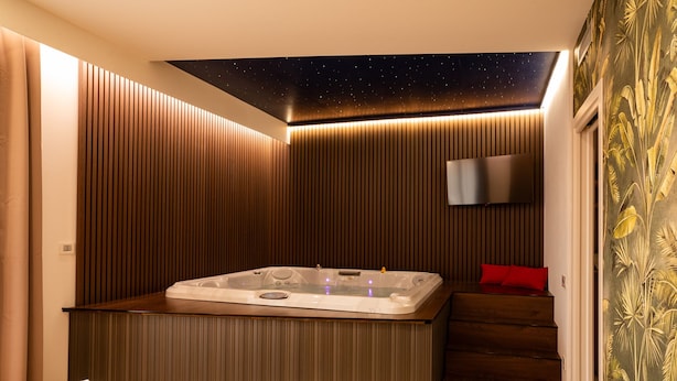 A modern bathroom with a freestanding bathtub, wooden paneling, a starry ceiling, and a television mounted on the wall.