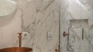 A modern bathroom with a marble wall, a copper sink, a toilet, and a glass-enclosed shower.