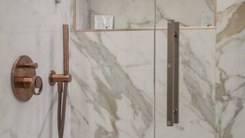 Un baño moderno con ducha envuelta en cristal, paredes de mármol y diseño minimalista.