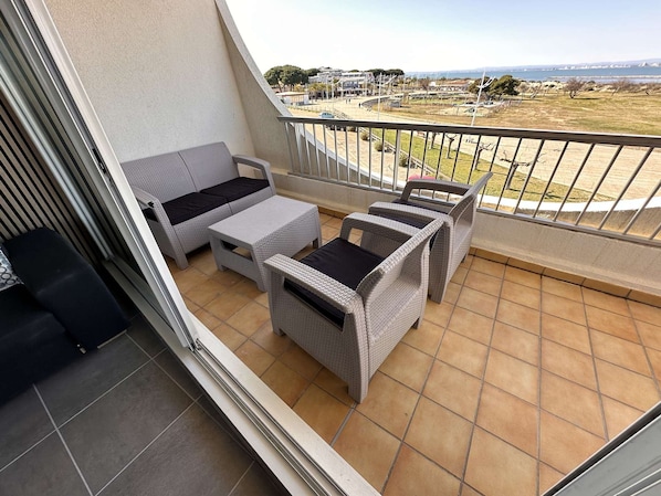 A balcony with wicker furniture and a view of a coastal area.