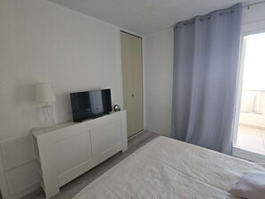 A hotel room with a bed, a television on a white cabinet, a door, and a window with curtains.