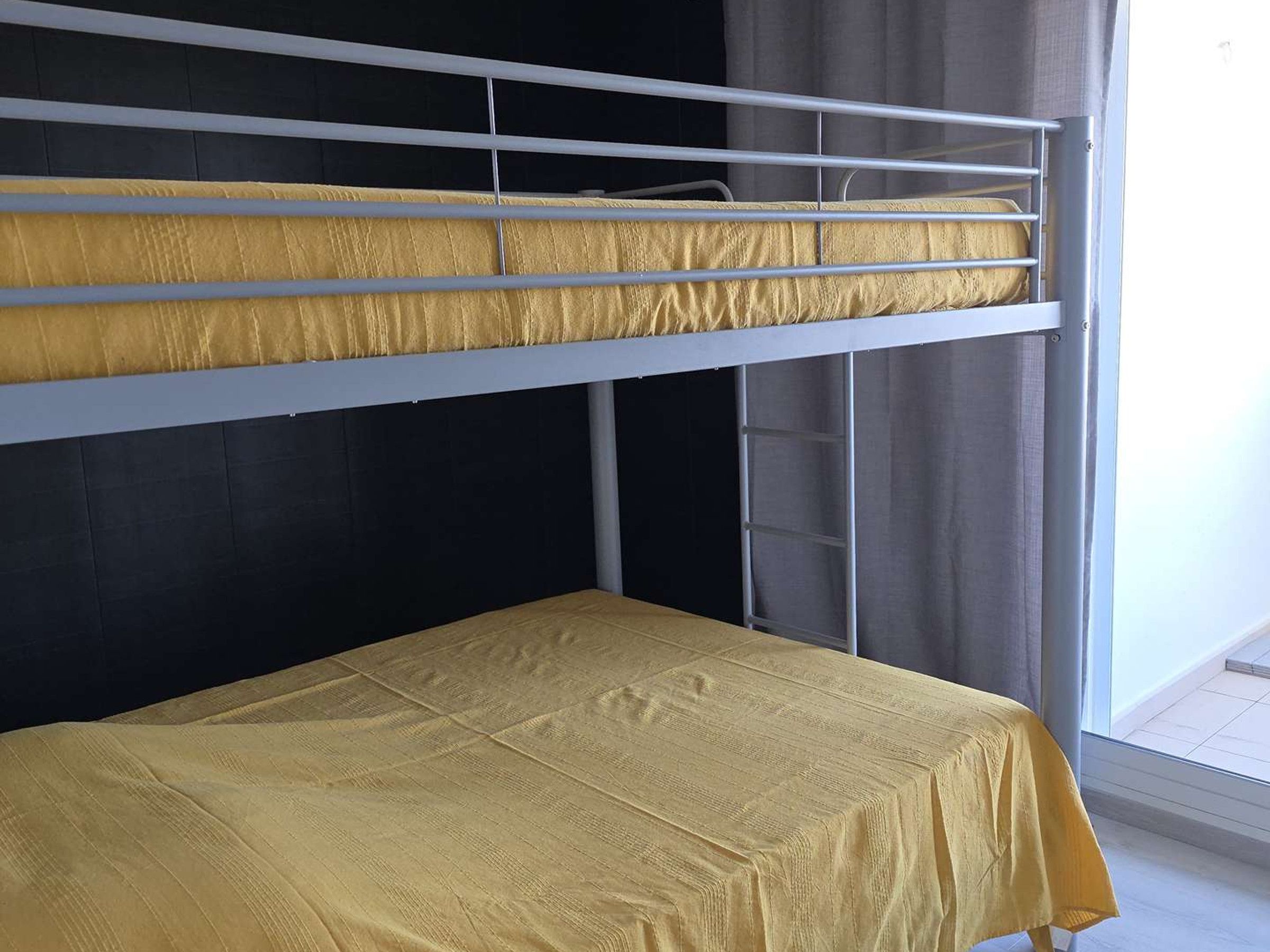 A bunk bed with a yellow mattress and a single bed below.