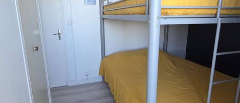 A bunk bed with a yellow mattress in a room with a white door and a small poster on the wall.