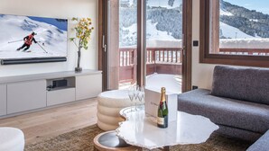 Ett modernt vardagsrum med en tv som visar skidrelaterat material, ett glasbord med en flaska och en soffa.