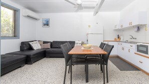 A modern kitchen with white cabinets, a wooden dining table, and a black sofa. - Koala Lodge - Unit 3 (ILUKA)