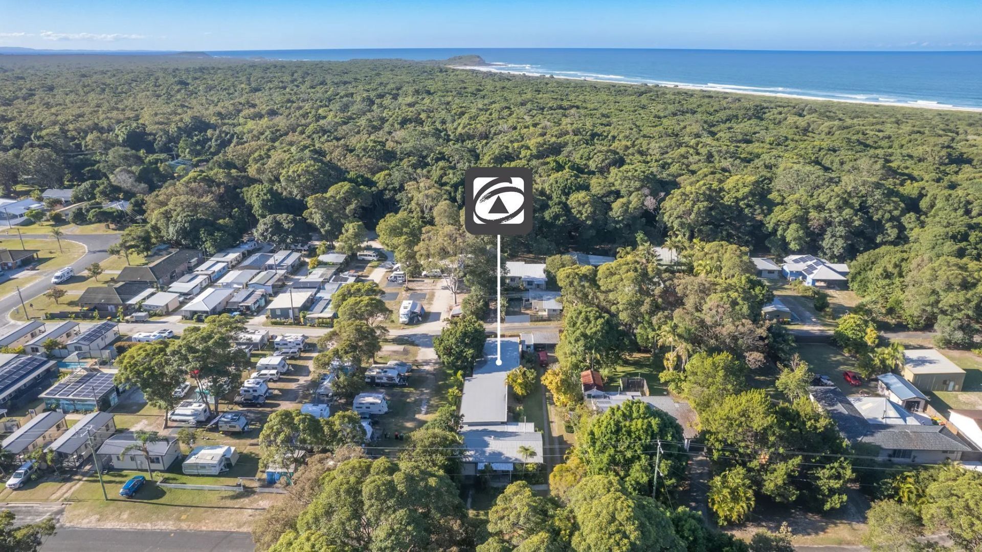 Vue aérienne d’un terrain de camping avec des camping-cars et des maisons mobiles, entouré d’une forêt dense et avec une plage en arrière-plan.