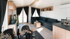 A modern living room with a dark green sofa, a wooden coffee table, and a dining area with a table set for two.